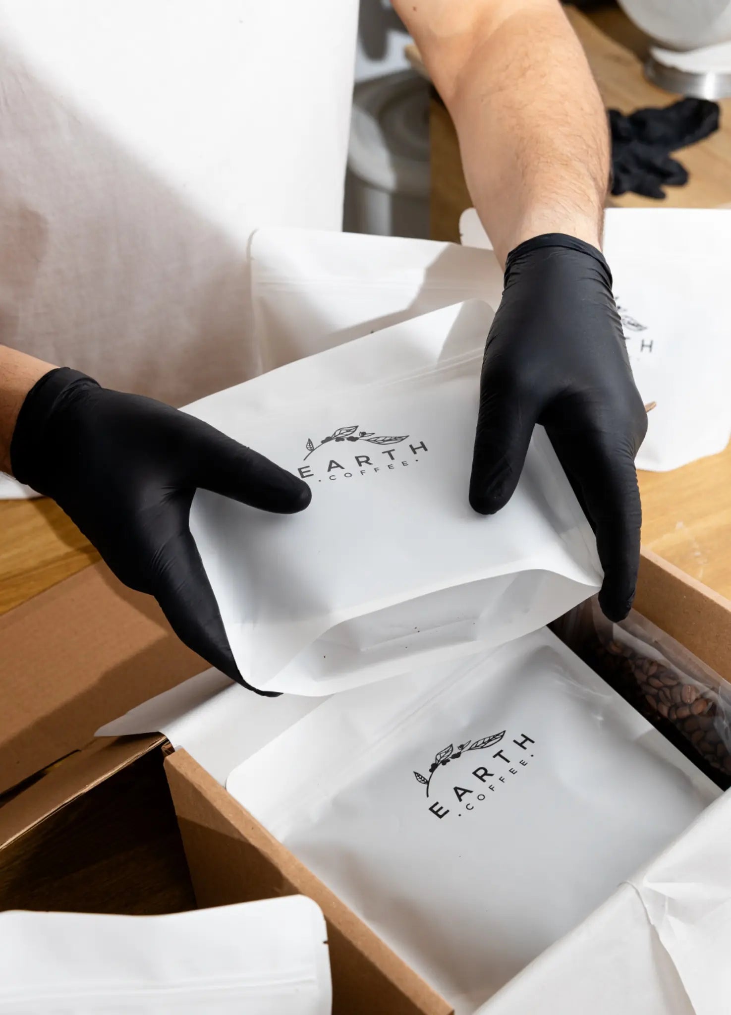 Person wearing black gloves handling white boxes with 'Earth' branding.